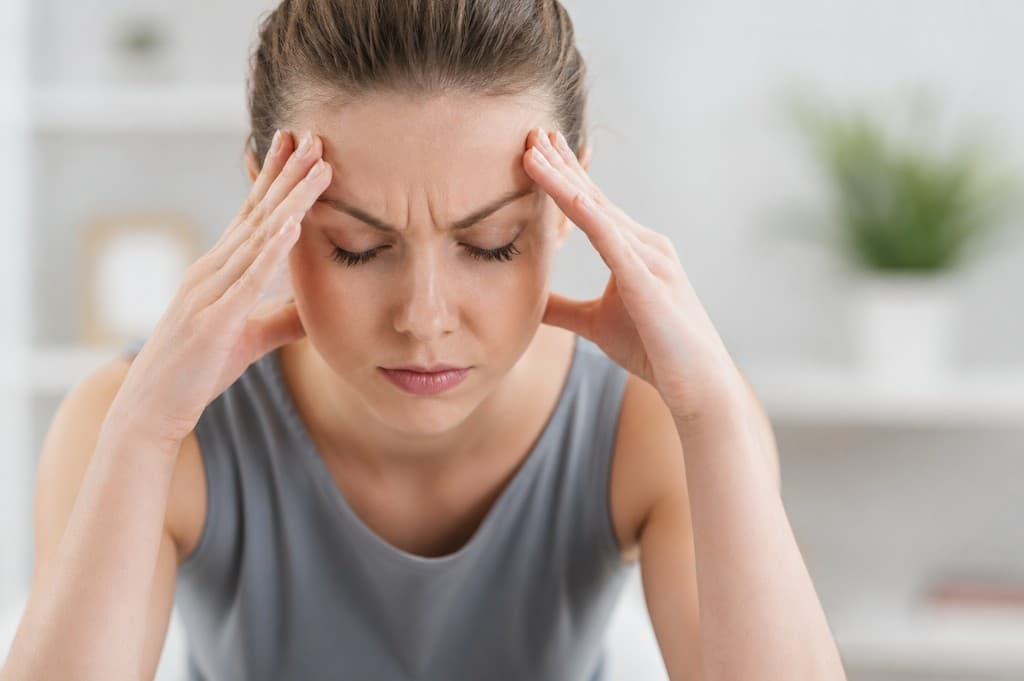 Patient experiencing migraine pain with hands on forehead